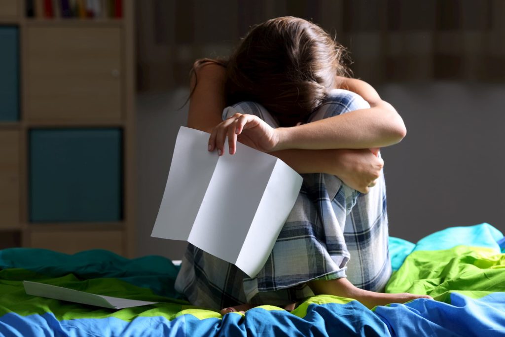 Krankheitsbedingte Kündigung - Traurige Frau sitzt auf einem Bett