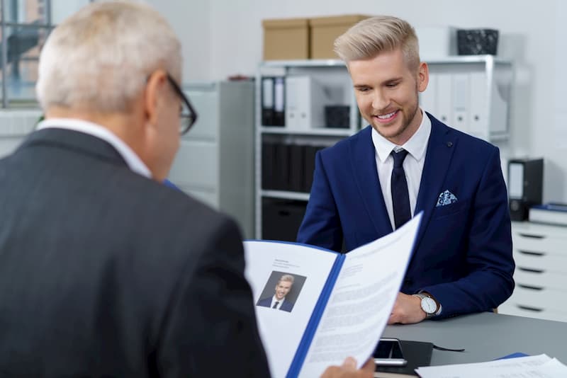 Ein Mann sitzt im Bewerbungsgespräch, der Personaler durchschaut den Curriculum Vitae