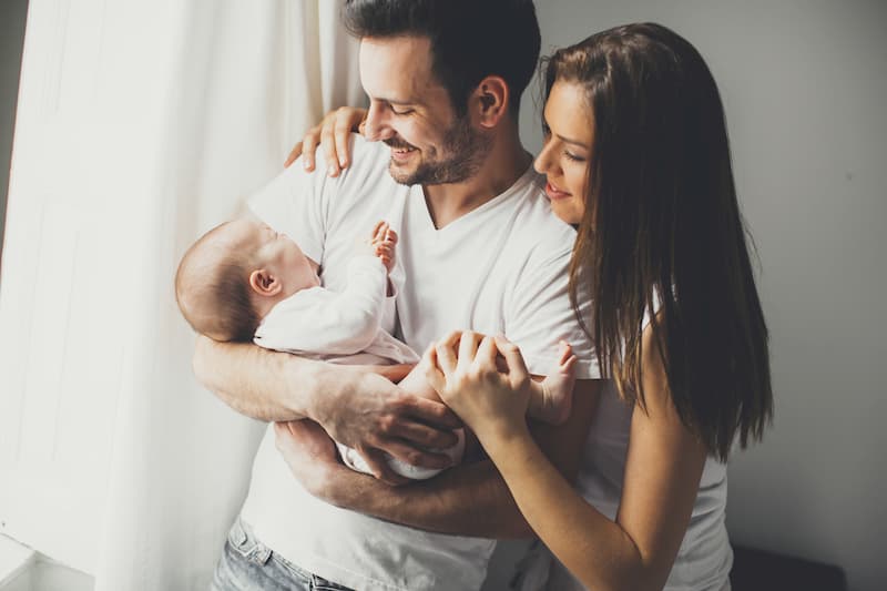 Glückliche Mutter und Vater mit Baby auf dem Arm. Während der Elternzeit sind sie durch den Kündigungsschutz abgesichert