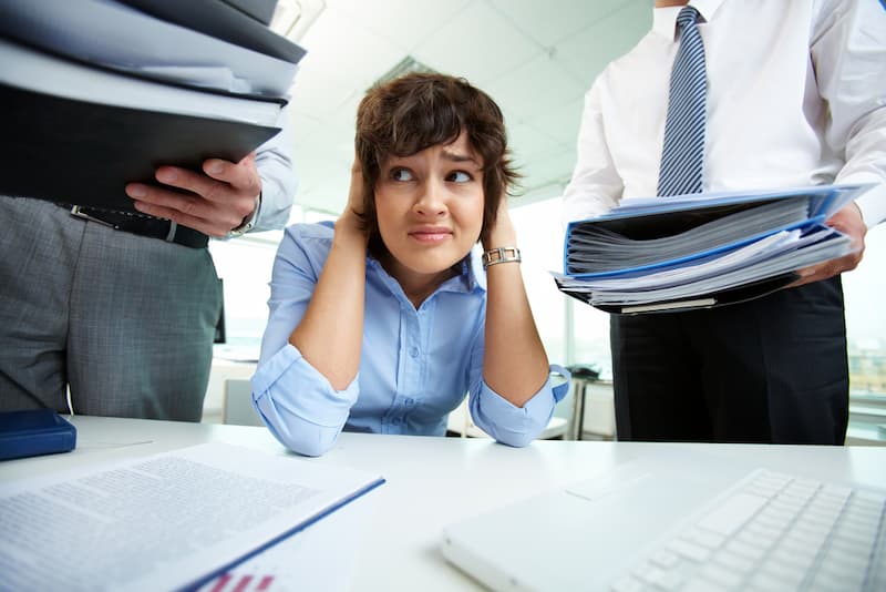 Eine Frau hält sich im Büro die Ohren zu, sie leidet unter Beleidigungen am Arbeitsplatz