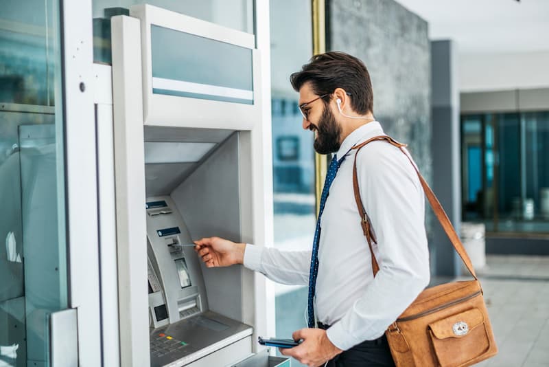 Ein Mann steht an einem Bankautomat und hebt sein Einstiegsgehalt ab
