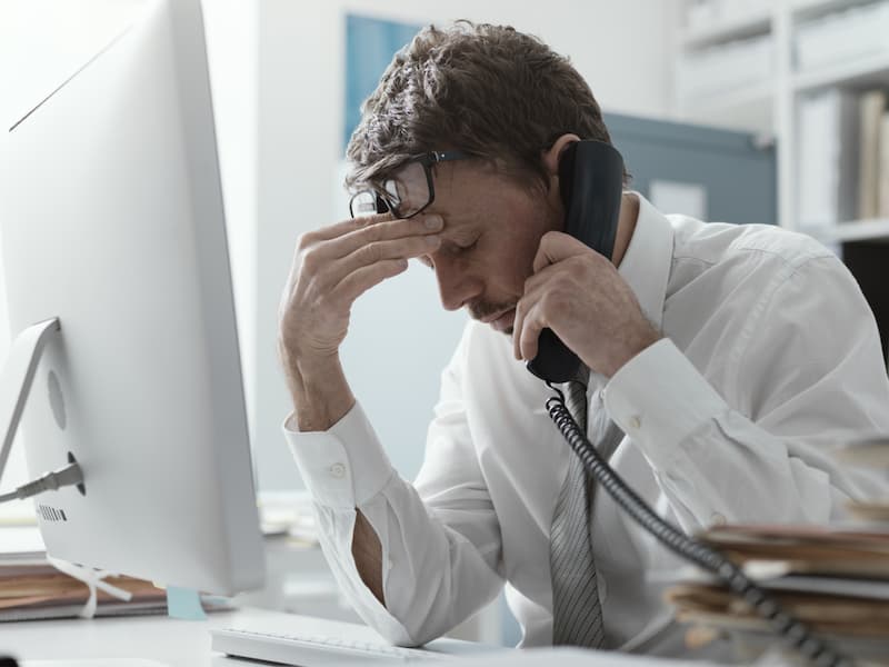 Ein Mann ist am Schreibtisch im Büro gestresst durch die Doppelbelastung von Familie und Beruf