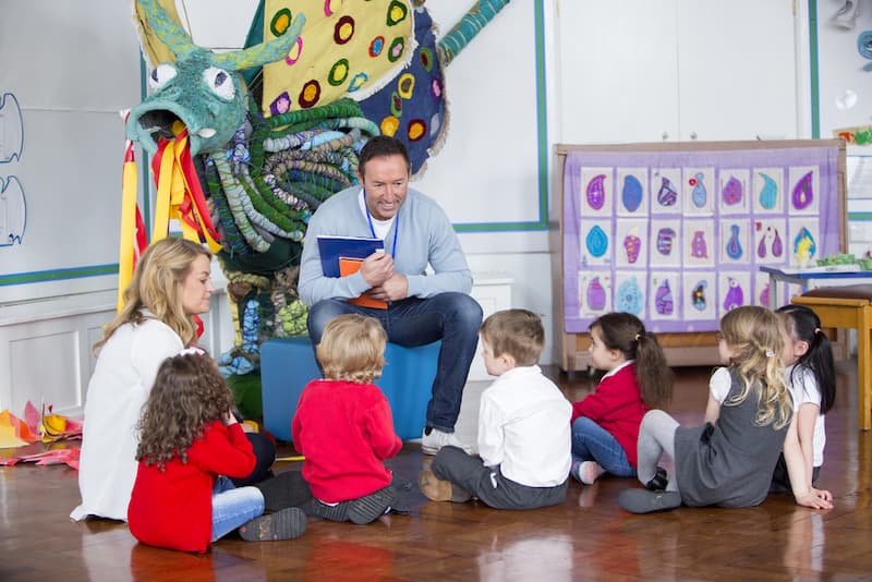 Ein Mann sitzt vor Kindern nach der Umschulung zum Erzieher