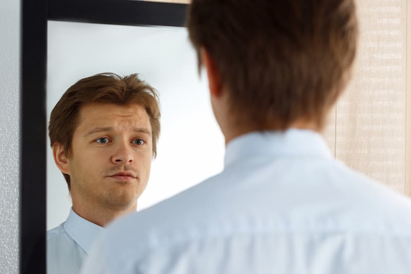 Ein Mann blickt in den Spiegel, was ist die richtige Dosierung für Selbstkritik?