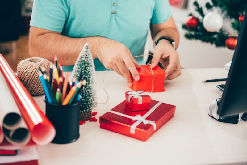 Ein Mitarbeiter verpackt ein kleines Weihnachtsgeschenk für einen Kollegen