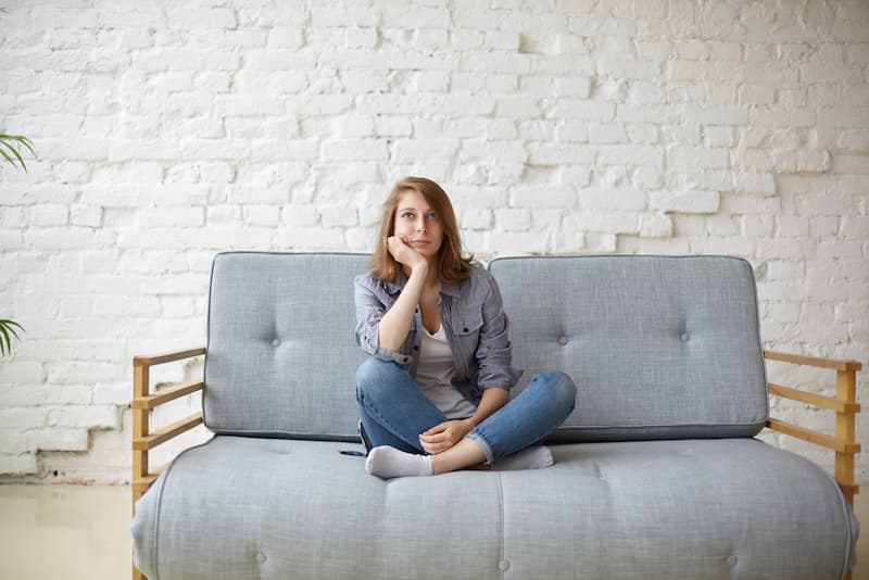 Eine Frau sitzt gelangweilt auf dem Sofa, wann sollte man aus dem Alltag ausbrechen?