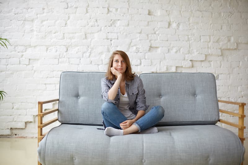 Eine Frau sitzt gelangweilt auf dem Sofa, wann sollte man aus dem Alltag ausbrechen?
