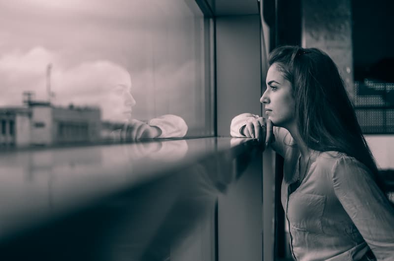 Eine Frau blickt aus dem Fenster, wie lässt sich Unsicherheit überwinden?