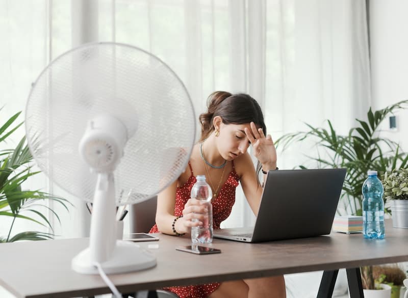 Eine Frau leidet unter Hitze am Arbeitsplatz, was steht im Arbeitsrecht?