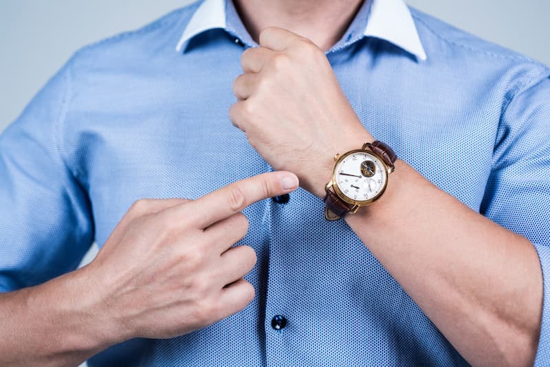 Ein Mann zeigt auf seine Armbanduhr, was ist Pünktlichkeit?