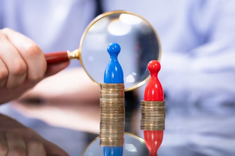 Zwei Figuren werden mit der Lupe betrachtet, was ist das Gender Pay Gap?