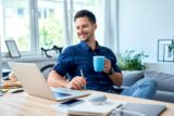 Mann sitzt zufrieden mit Kaffeetasse vor Schreibtisch