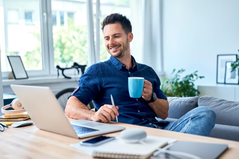 Mann sitzt zufrieden mit Kaffeetasse vor Schreibtisch