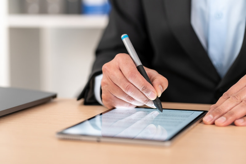Den Arbeitsvertrag digital unterschreiben: Geht das? 2 Ein Mann im Anzug möchte seinen Arbeitsvertrag digital unterschreiben. Dafür nutzt er ein Tablet und einen Stift.