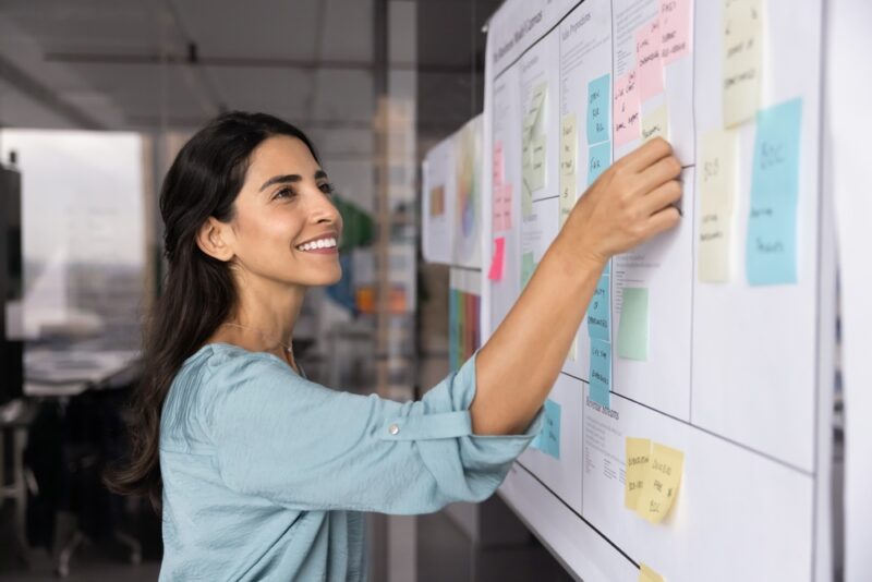 Kompetenzprofil für die Bewerbung: Was es ist & wie du es nutzt 2 Junge Frau organisiert Post-Its auf einem Whiteboard.